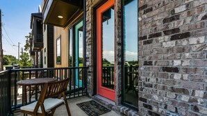 A balcony with a table and chairs, a red door, and a brick wall. - Bushwacker - European flare in downtown Pensacola (Pensacola)