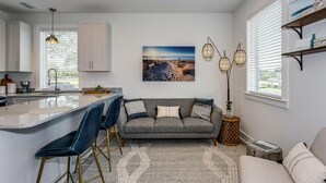 A modern kitchen with a central island, bar stools, a grey sofa, and a patterned rug. - Bushwacker - European flare in downtown Pensacola (Pensacola)