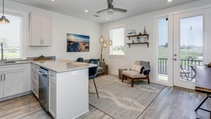 A modern kitchen with a central island, a dining area with a sofa and chairs, a ceiling fan, and a view of the outdoors through a glass door. - Bushwacker - European flare in downtown Pensacola (Pensacola)