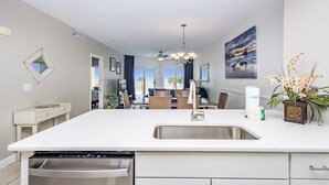 A modern kitchen with a central island, a built-in dishwasher, and a view to a dining area with a view of the outdoors.
