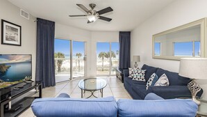 A modern living room with a blue sofa, a glass coffee table, a ceiling fan, and a television.