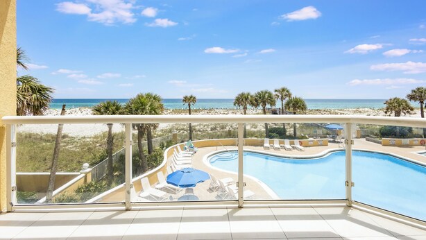 A balcony with a view of a beach and a swimming pool.