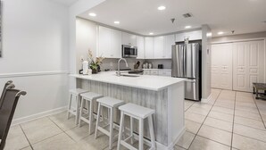 A modern kitchen with white cabinetry, a central island with bar stools, stainless steel appliances, and recessed ceiling lighting.