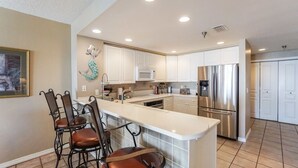 A modern kitchen with white cabinets, stainless steel appliances, and a central island with bar stools. - Great Location! Stunning Gulf Front Views at Emerald Isle! (Pensacola Beach)