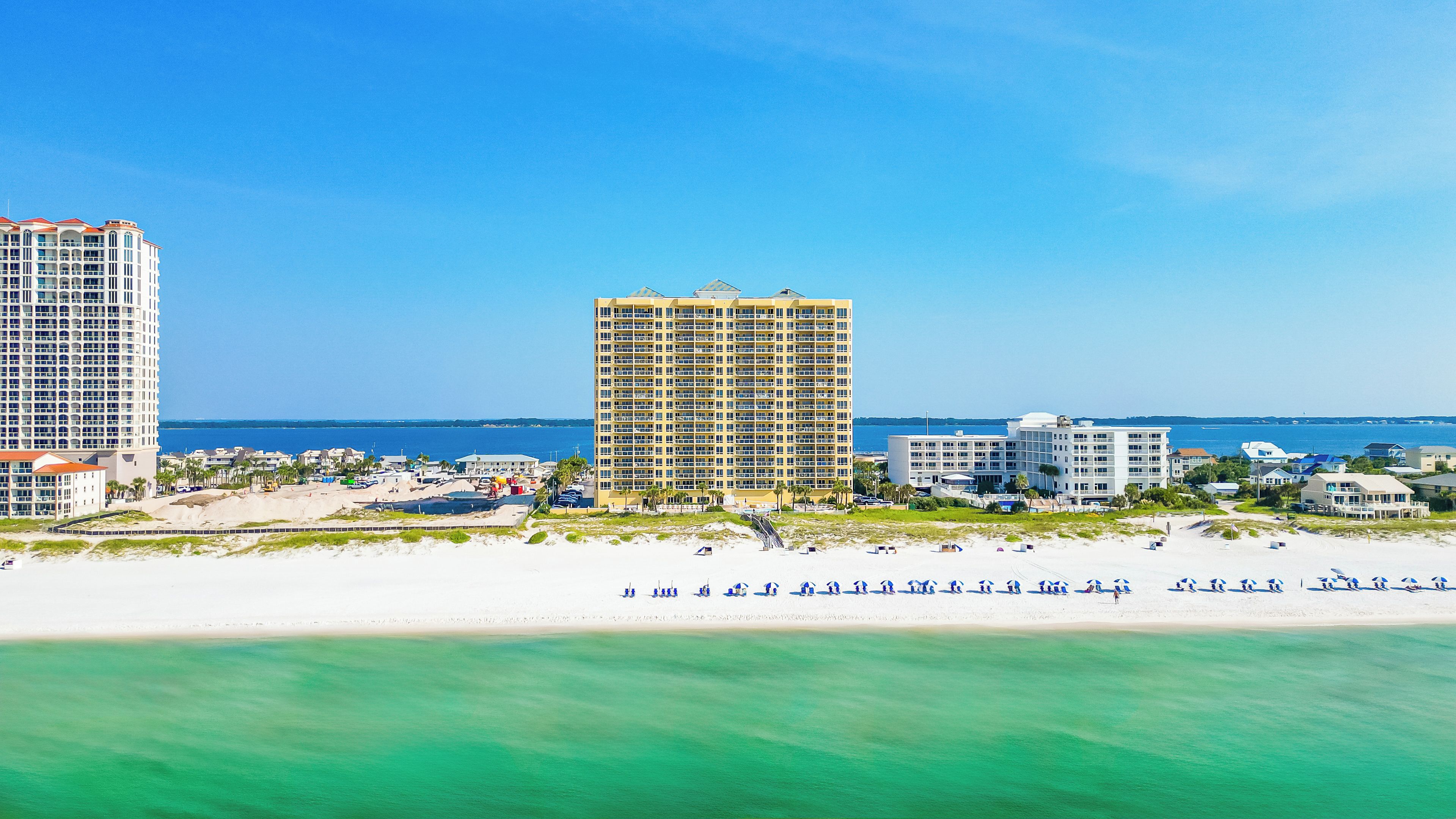 A coastal hotel with multiple high-rise buildings, a beach, and clear blue skies.