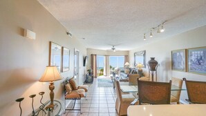 A spacious living area with a high ceiling, large windows, and a view of the outdoors. There are multiple seating areas with sofas and chairs, and a dining table. - Great Location! Stunning Gulf Front Views at Emerald Isle! (Pensacola Beach)