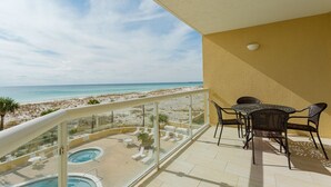Un balcón con vista a la playa y al océano, una piscina y mobiliario de exterior.
