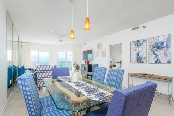 A modern dining area with a glass table and blue-striped chairs, overlooking a scenic view.
