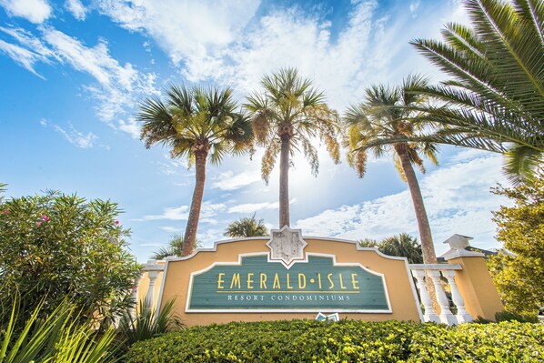 A sign for Emerald Isle Resort Condominiums with palm trees and a clear sky in the background.