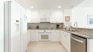 Una cocina moderna con armarios blancos, microondas integrado, lavavajillas y encimera de granito.