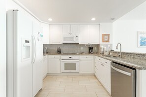 A modern kitchen with white cabinets, a built-in microwave, a dishwasher, and a granite countertop.