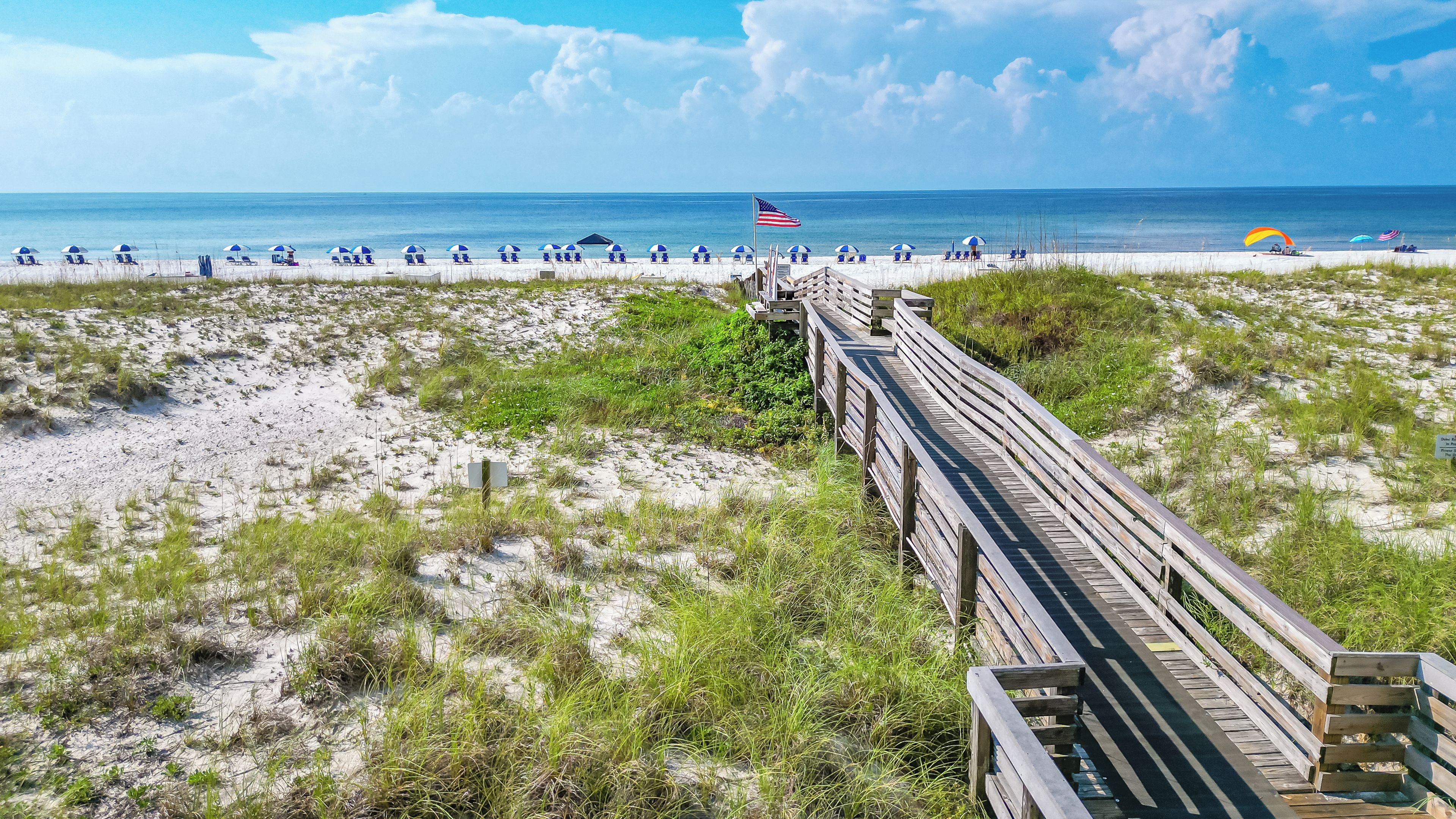 A beach with a wooden boardwalk leading to beach chairs and umbrellas.