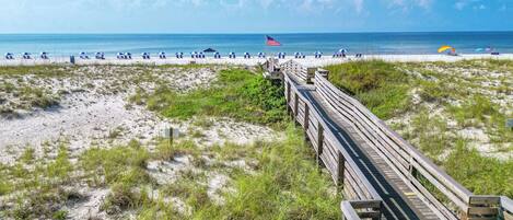 A beach with a wooden boardwalk leading to beach chairs and umbrellas.