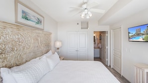 Un dormitorio con una cama grande, un ventilador de techo, un televisor y una puerta que da a un baño.