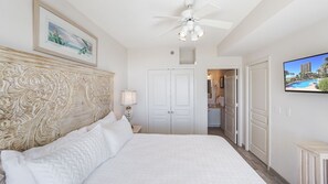 Une chambre avec un grand lit, un ventilateur de plafond, une télévision et une porte donnant sur une salle de bain.