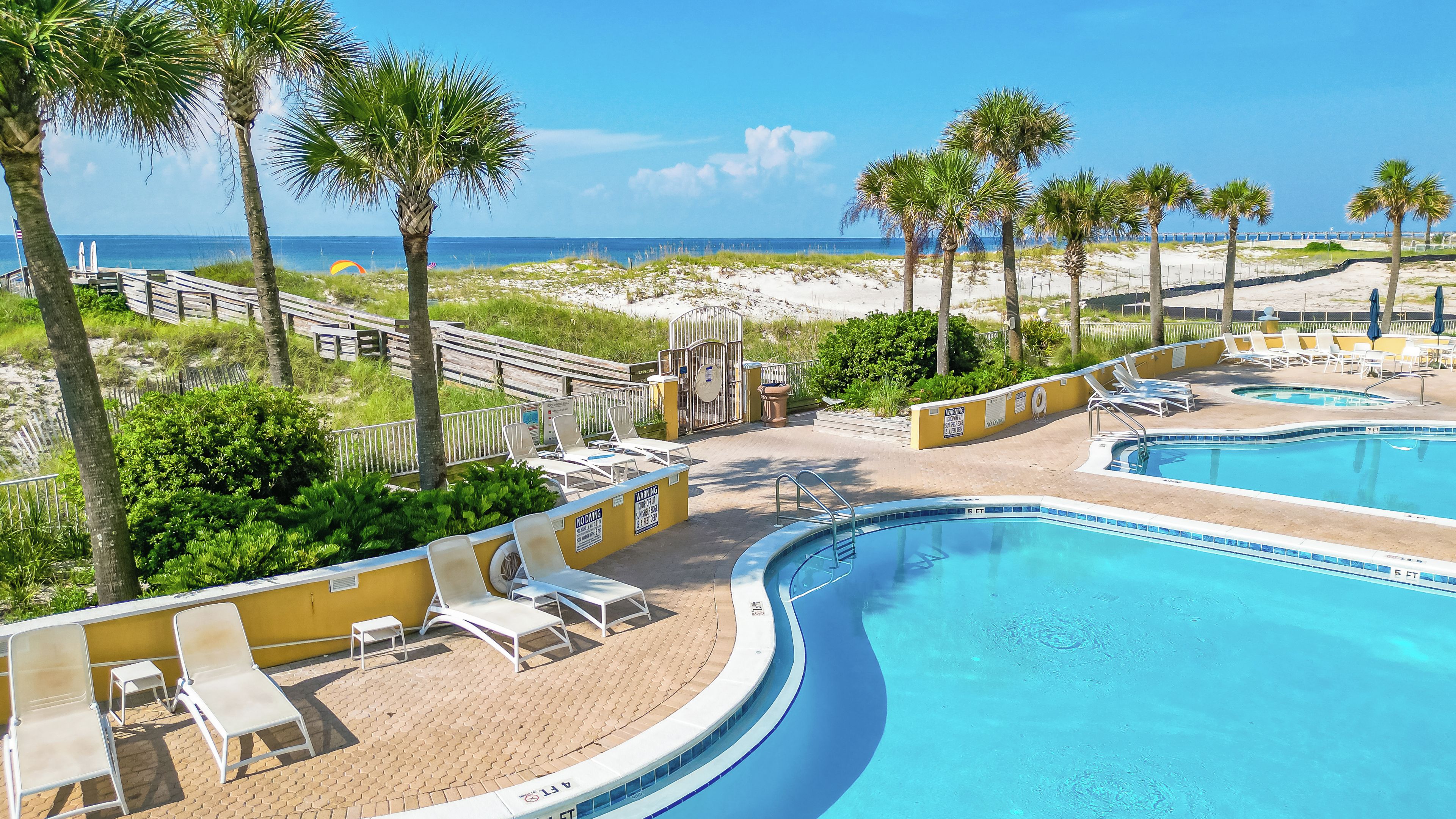 A pool area with lounge chairs, a wooden deck, and a view of the beach.