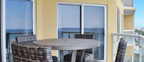 A balcony with wicker furniture, large windows, and a view of the sea.