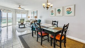 A dining area with a glass table, chairs, a chandelier, and artwork on the walls. - Great Rates at Emerald Isle 506 - 2B Gulf Front Views! (Pensacola Beach)
