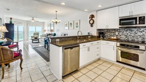 A modern kitchen with white cabinets, a granite countertop, stainless steel appliances, and a view to the outside. - Great Rates at Emerald Isle 506 - 2B Gulf Front Views! (Pensacola Beach)