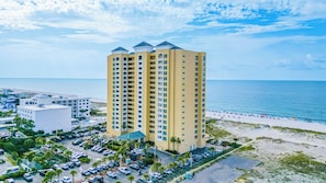 A high-rise hotel with multiple balconies, a parking lot, and a beach view.