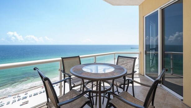 A balcony with a round table and chairs, overlooking a beach and the ocean.