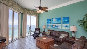 A living room with a view of the ocean, a ceiling fan, and a large window.