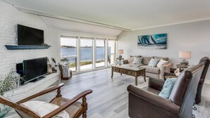 A spacious living room with a large window overlooking a body of water, a fireplace, and a comfortable seating area. - Bay Front- Water Access- 3B/ Great for Families! (Pensacola Beach)