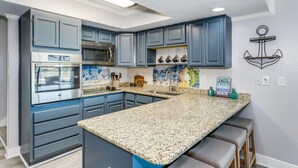 A kitchen with blue cabinets, a granite countertop, a stainless steel oven, and a hanging light fixture. - Bay Front- Water Access- 3B/ Great for Families! (Pensacola Beach)