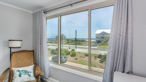 A room with a large window, a wicker chair with a turtle pillow, and a lamp. - Bay Front- Water Access- 3B/ Great for Families! (Pensacola Beach)