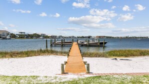 A wooden pier leading to a dock with boats, a sandy beach, and houses in the background. - Bay Front- Water Access- 3B/ Great for Families! (Pensacola Beach)