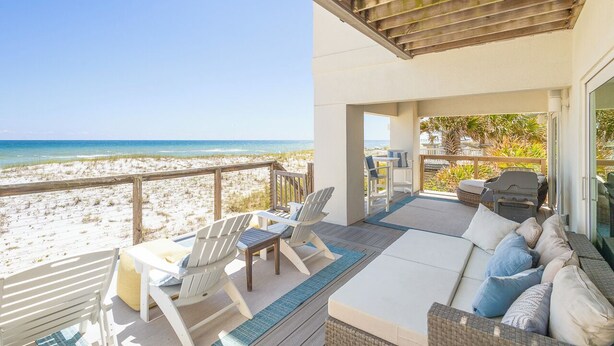Eine Terrasse am Strand mit einer Couch, Stühlen und einem Tisch mit Blick aufs Meer.