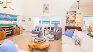 Ein geräumiges Wohnzimmer mit großem Fernseher, bequemen Sitzgelegenheiten und Blick auf den Strand.