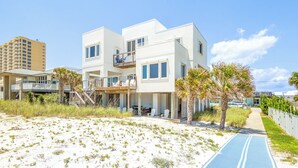 Ein Anwesen direkt am Strand mit einem zweigeschossigen Gebäude, einer überdachten Terrasse und einem Weg zum Strand.