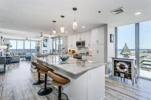 A modern kitchen with a large island, bar stools, and a view of the beach.