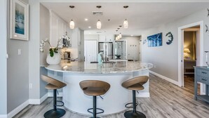 Una cocina moderna con una isla central, taburetes de bar, iluminación colgante y vista al área del comedor.