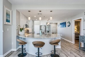 A modern kitchen with a central island, bar stools, pendant lighting, and a view into the dining area.