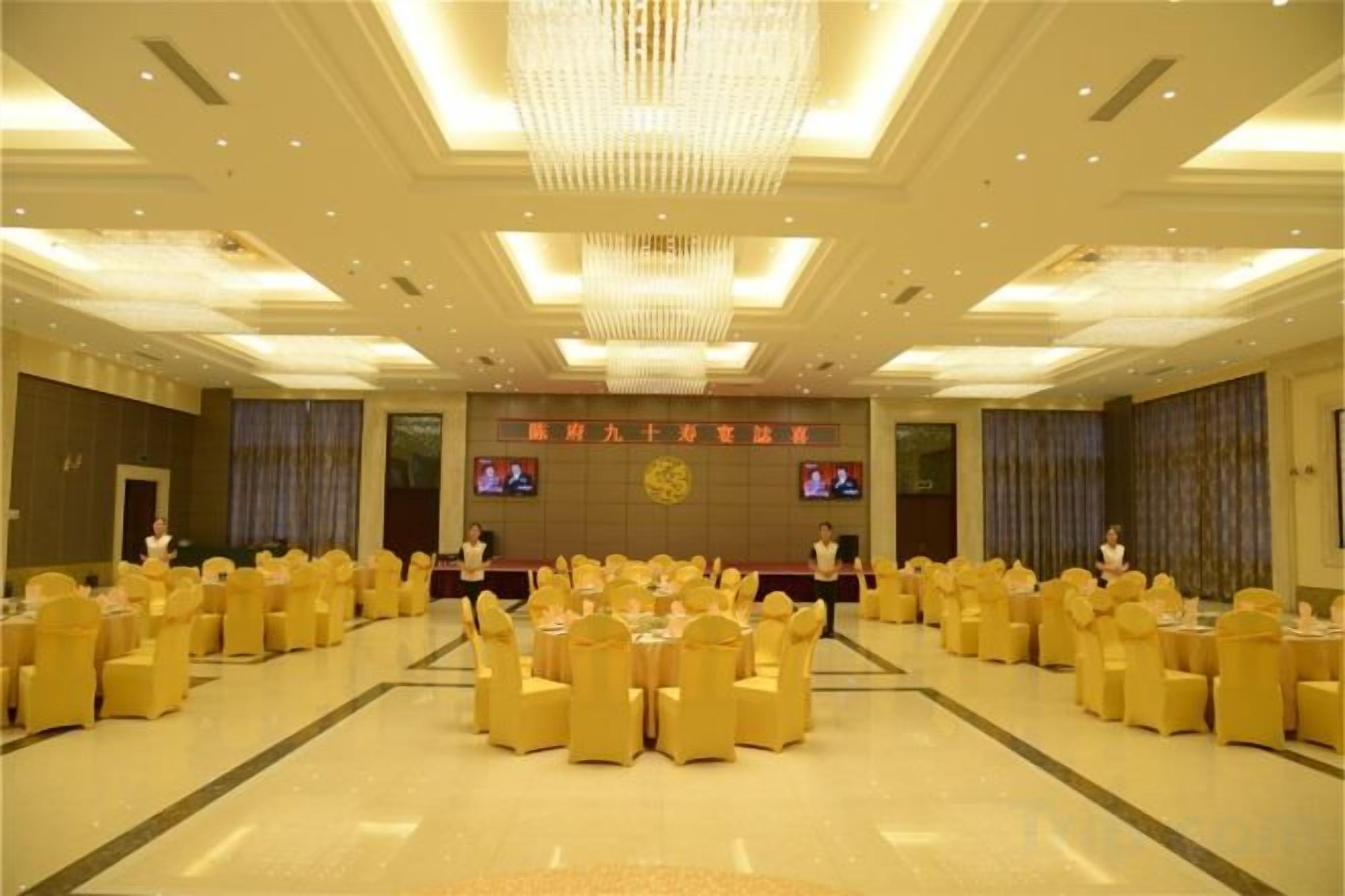 A banquet hall with round tables and chairs, a stage with a podium, and a chandelier.