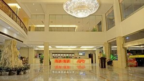 Un vestíbulo de hotel con candelabro, mostrador de recepción y una planta.