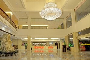 Un hall d’hôtel avec un lustre, un comptoir d’accueil et une plante.