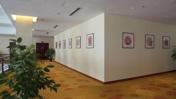 A hotel corridor with framed artwork on the walls, a carpeted floor, and a potted plant.