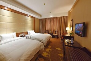 Habitación de hotel con dos camas, un escritorio con silla, un televisor y un ventanal con cortinas.