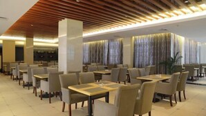 Un comedor moderno con varias mesas y sillas, paneles de techo de madera y ventanas amplias con cortinas.