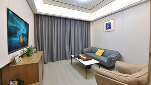 Una sala de estar moderna con un sofá azul, un sillón beige, una mesa de centro, un televisor y una lámpara de techo.