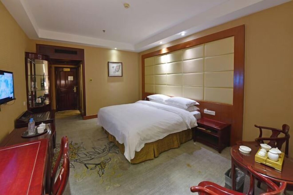 Habitación de hotel con cama, mesita de noche, televisor y espejo.