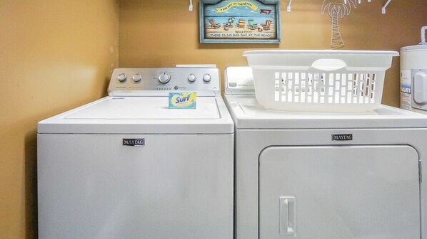 A laundry area with two Maytag washers and dryers, a white basket on the dryer, and a wall decoration.
