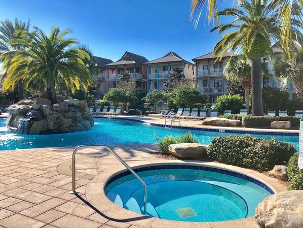 Une piscine avec un petit jacuzzi, entourée de chaises longues et de palmiers.
