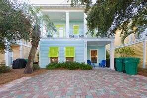 A two-story building with a covered patio area, a covered grill, and a trash bin.