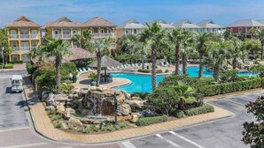 A resort with multiple-story buildings, a central swimming pool, palm trees, and a waterfall feature.