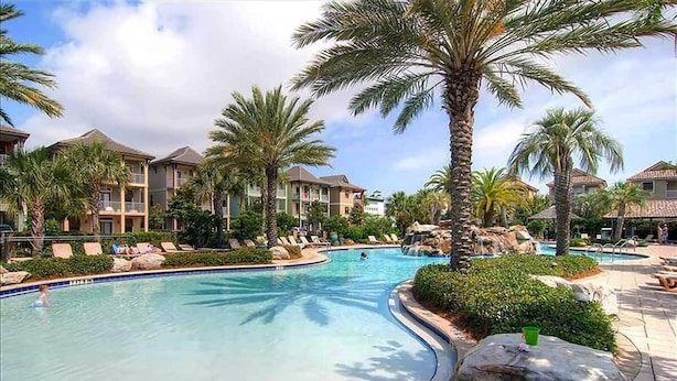 A resort pool area with palm trees, lounge chairs, and a clear blue pool.
