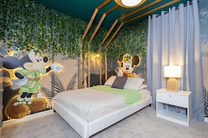 Un dormitorio con cama, mesita de noche y un mural de Mickey Mouse.